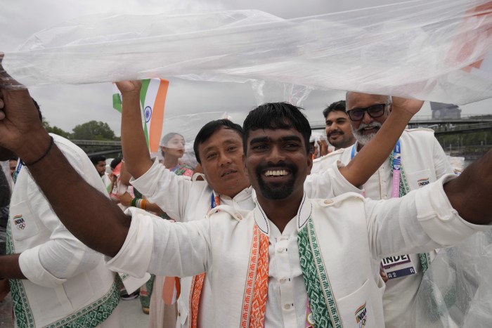 Indian athletes use a plastic sheet to cover themselves from rain as they travel in a boat on the Seine River in Paris, France, during the opening ceremony of the 2024 Summer Olympics, Friday, July 26, 2024.